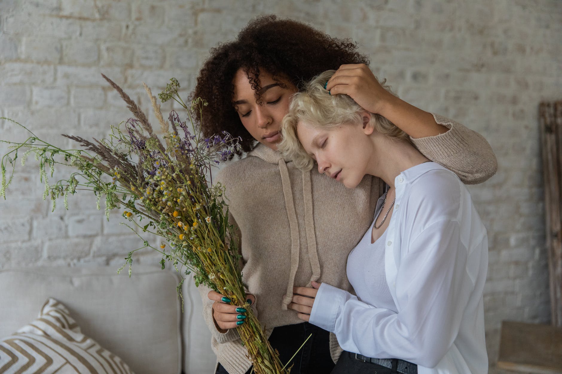 multiracial women with closed eyes hugging in room